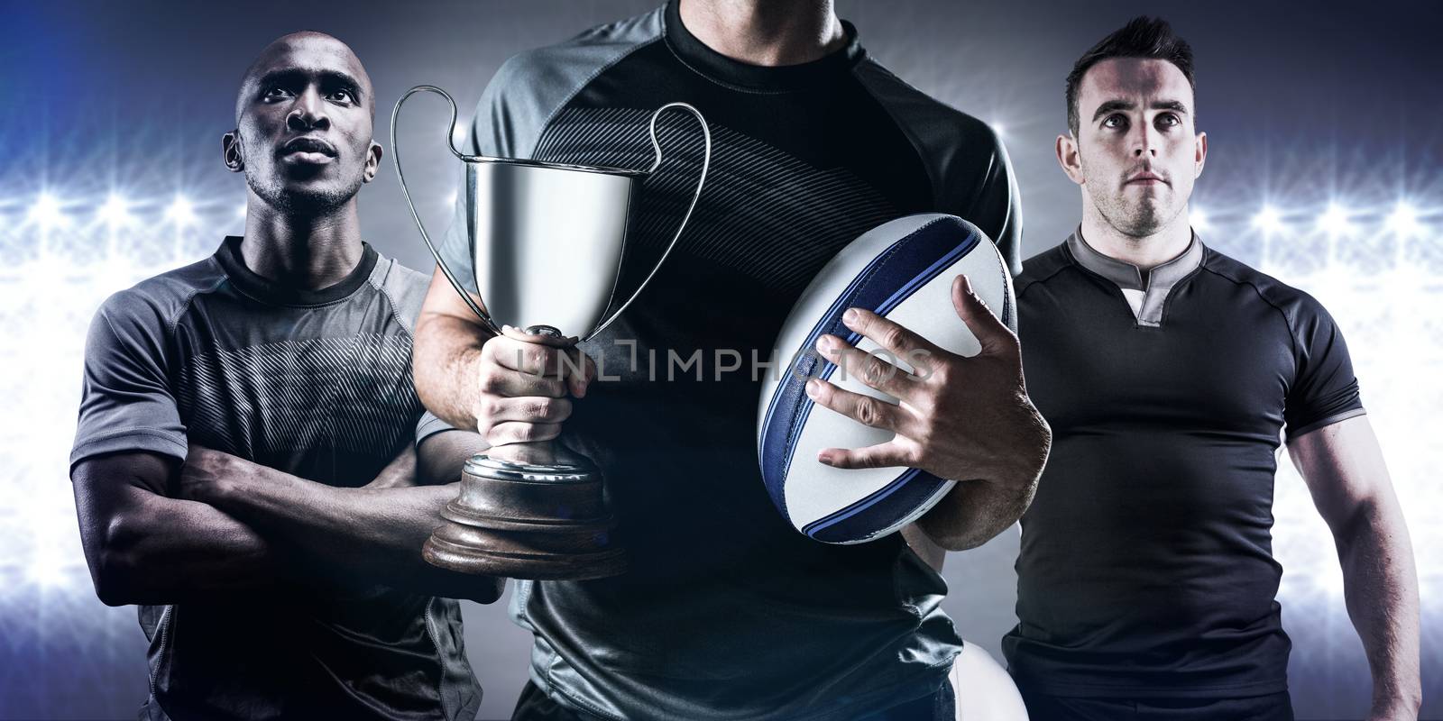 Midsection of successful rugby player holding trophy and ball against spotlight