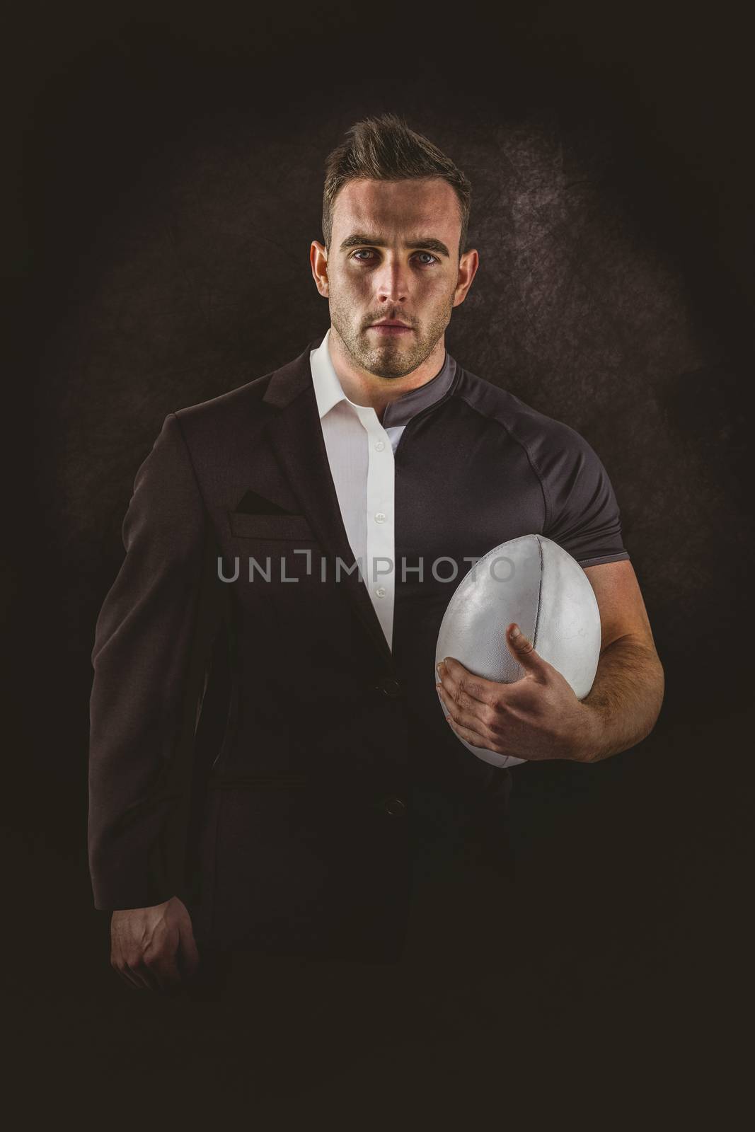 Tough rugby player holding ball against half a suit