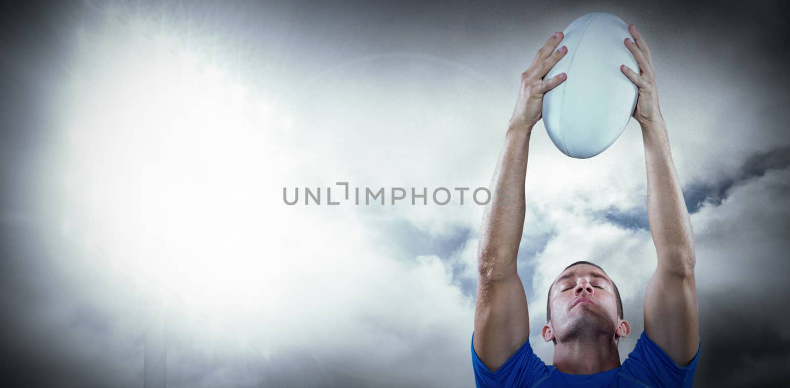 Rugby player holding ball with eyes closed against spotlight in sky