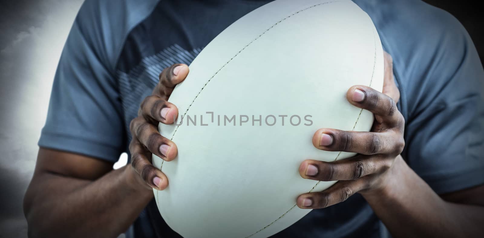 Mid section of sportsman holding rugby ball against spotlight in sky