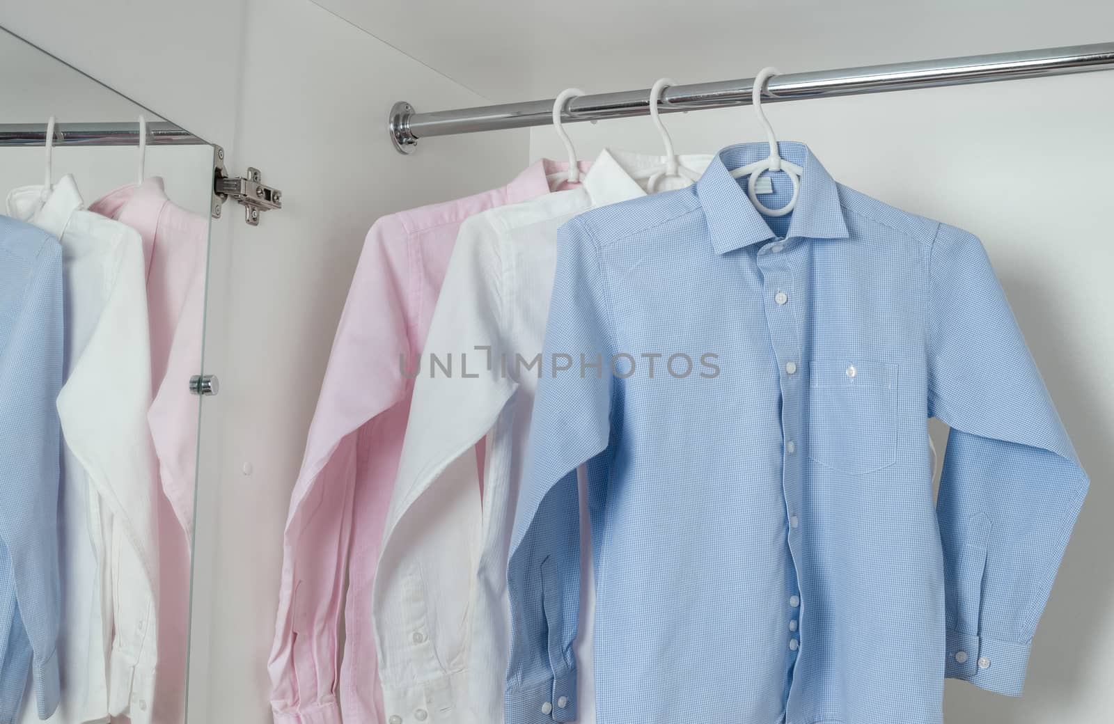 white, blue and pink clean ironed men's shirts hanging on hangers in the white wardrobe