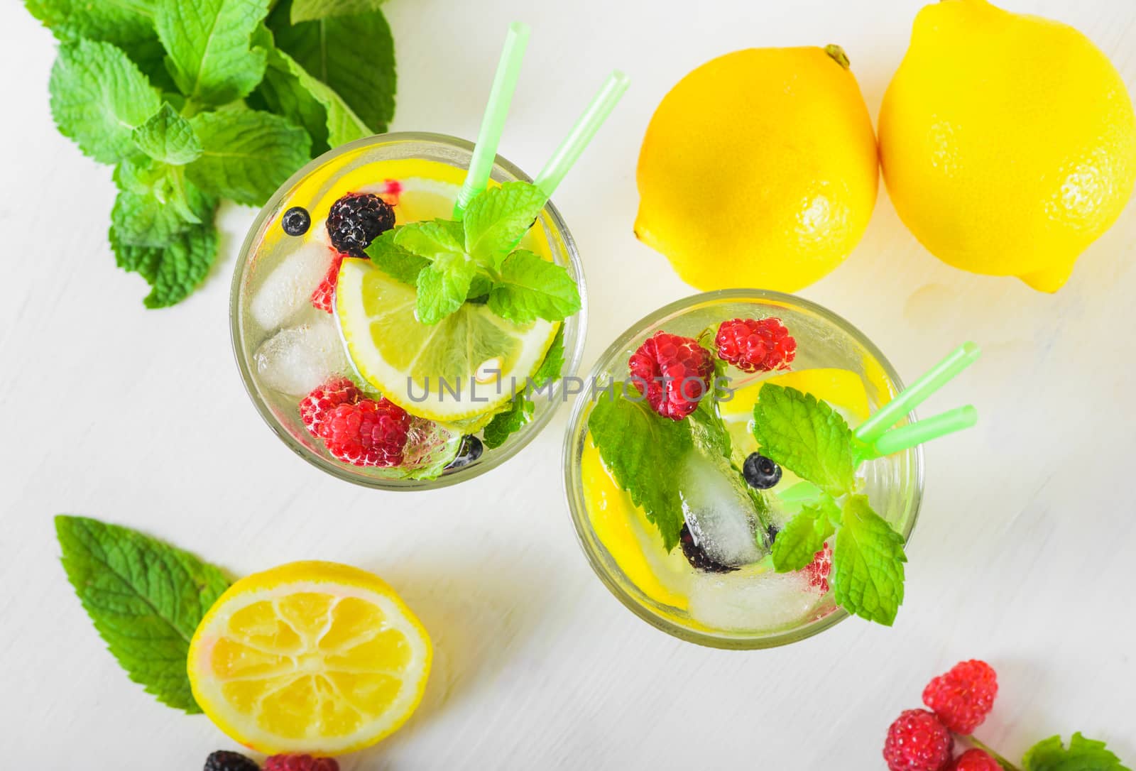 Delicious refreshing lemonade with fresh mint, Lemon, honey and ice decorated with raspberries, blueberries and blackberries on a white wooden table, close up. Healthy summer drink. Top view