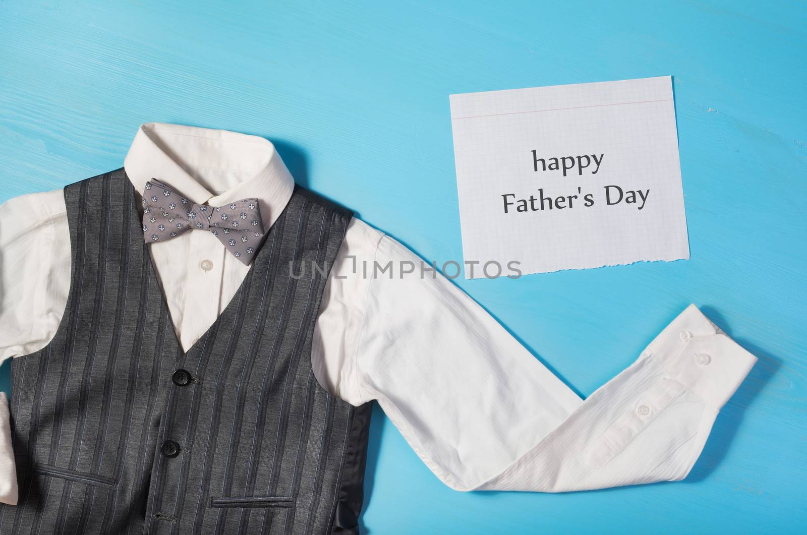 white shirt, gray vest and a bow tie and a sheet of paper with text  happy Father's Day on a bright blue background