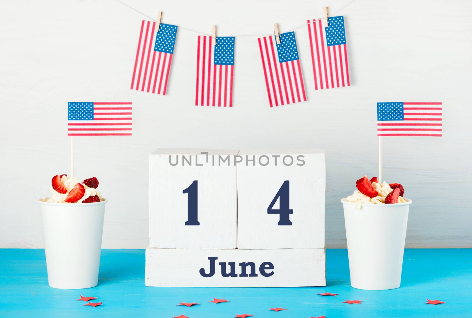 Greeting card on the day of the American flag, two desserts with cream, strawberries and American flags, perpetual calendar with the words June 14 , American flags hanging on a rope with clothespins 