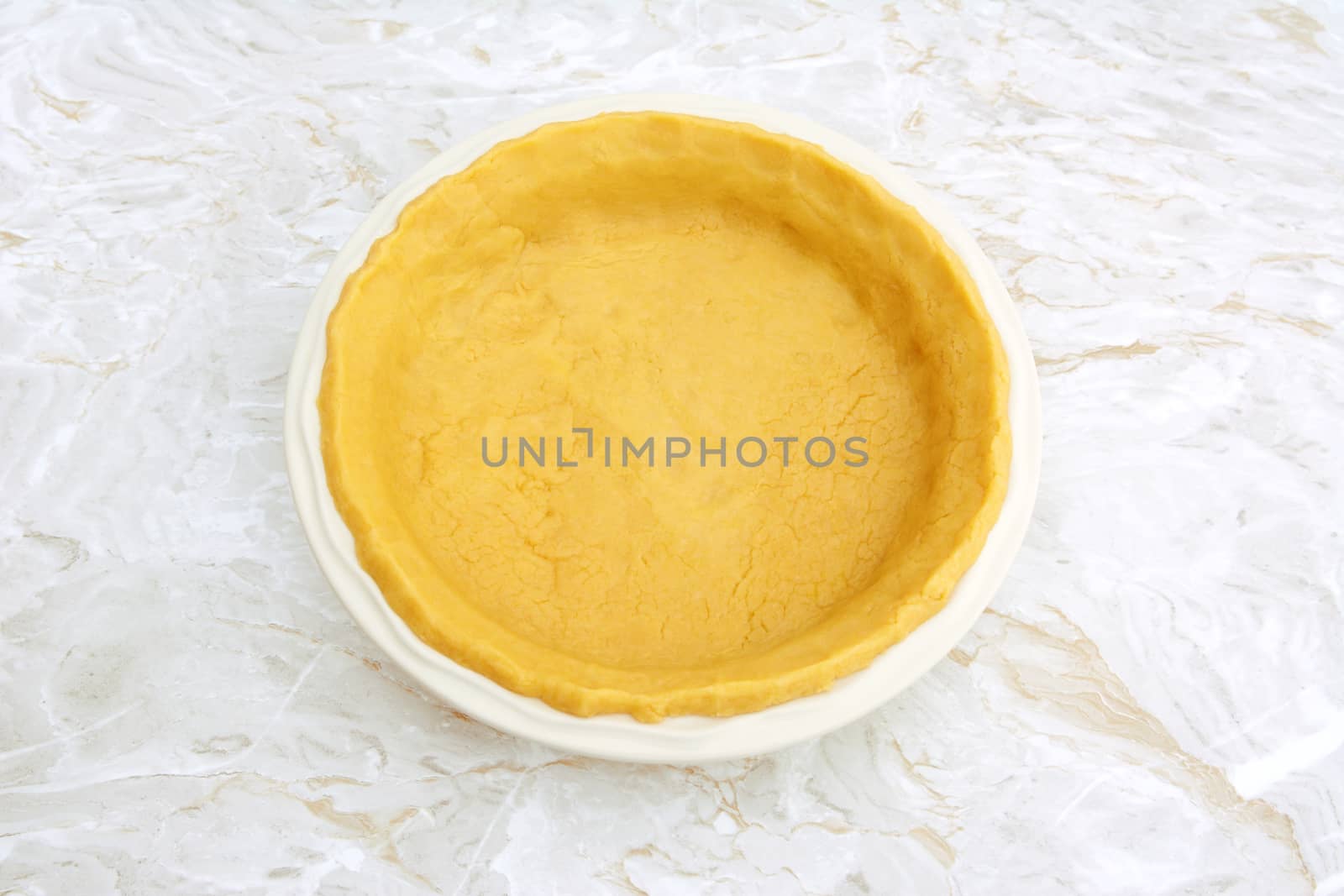 Circular ceramic pie dish lined with homemade pastry on a kitchen work surface