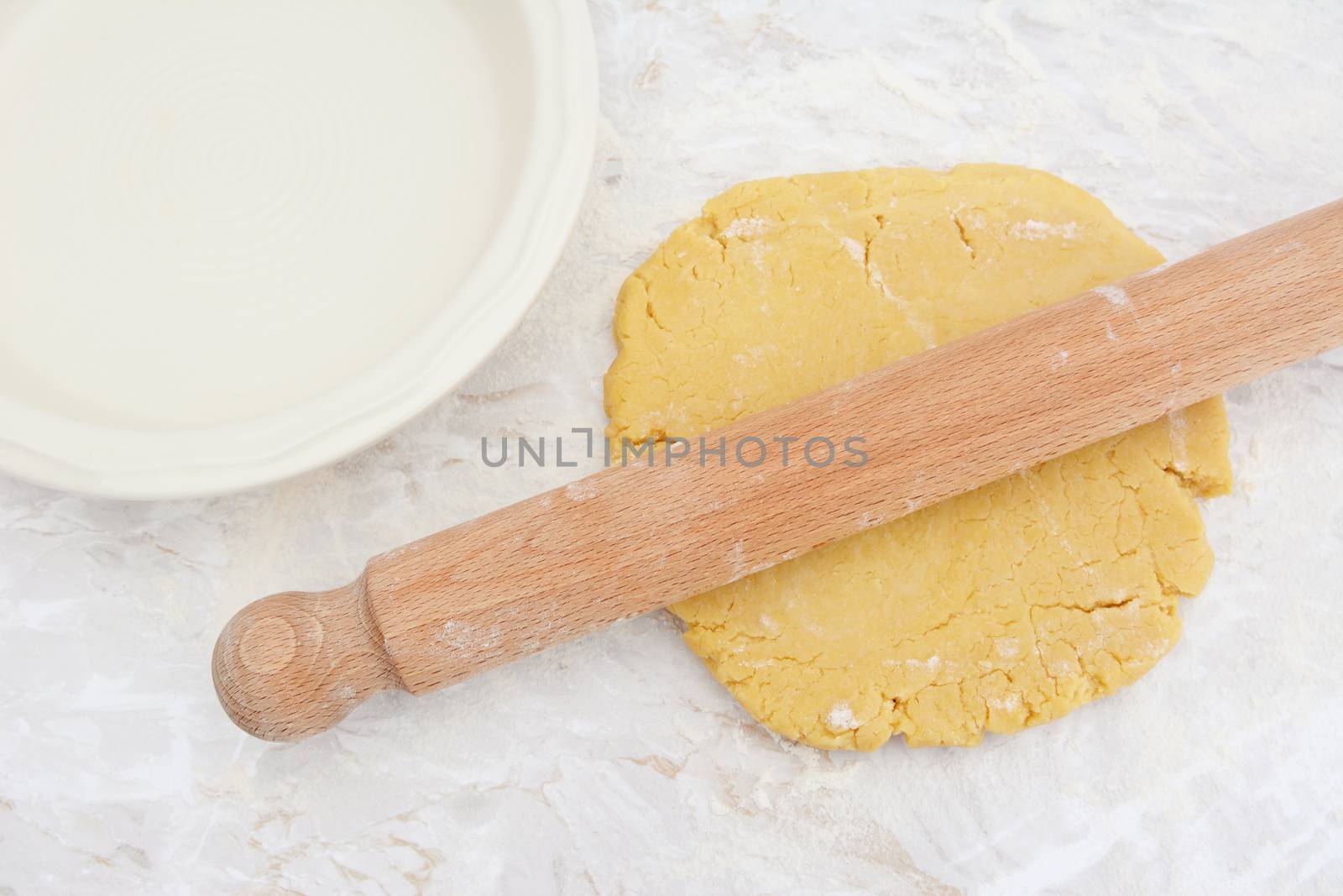 Rolling out homemade pastry with a wooden rolling pin next to a ceramic pie dish