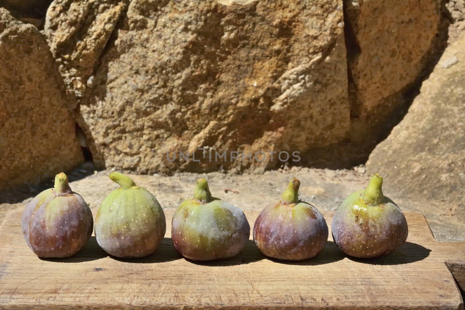 Composition of fig fruits on a wooden board and rocks in the background. 