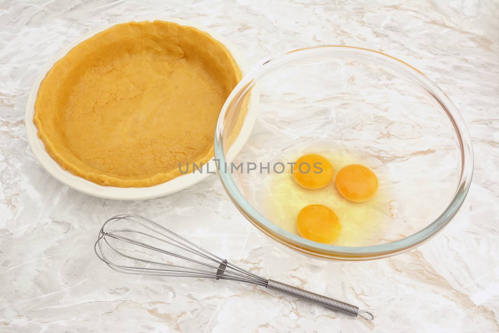 Bowl of raw eggs with a wire whisk and a pie dish lined with shortcrust pastry