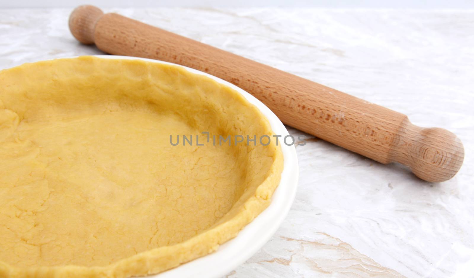 Pie dish lined with shortcrust pastry with wooden rolling pin on kitchen work surface