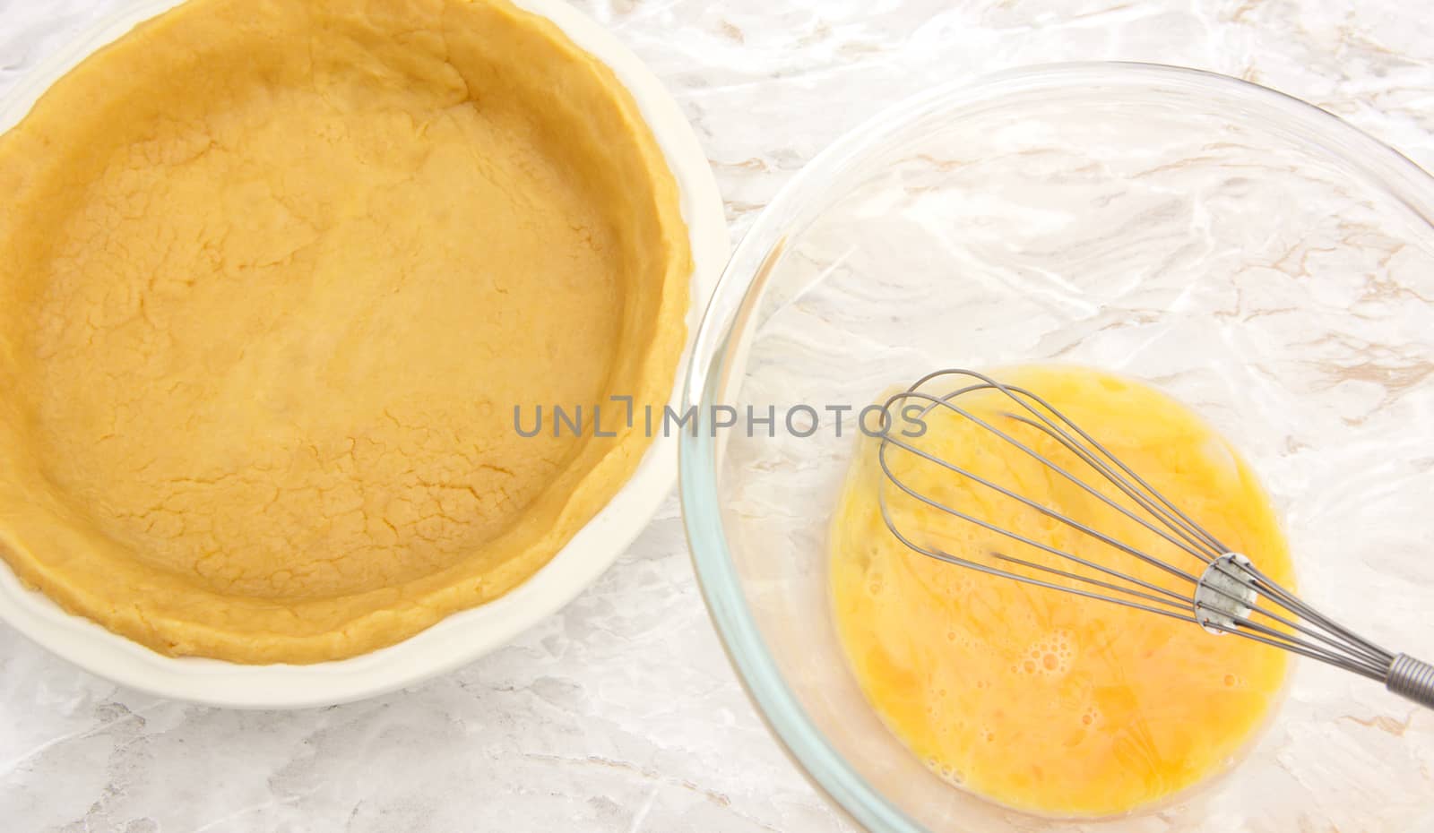 Ceramic pie dish lined with shortcrust pastry next to bowl of beaten eggs