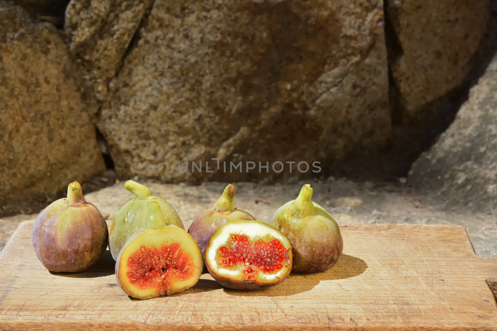 Composition of fig fruits on a wooden board and rocks in the background.