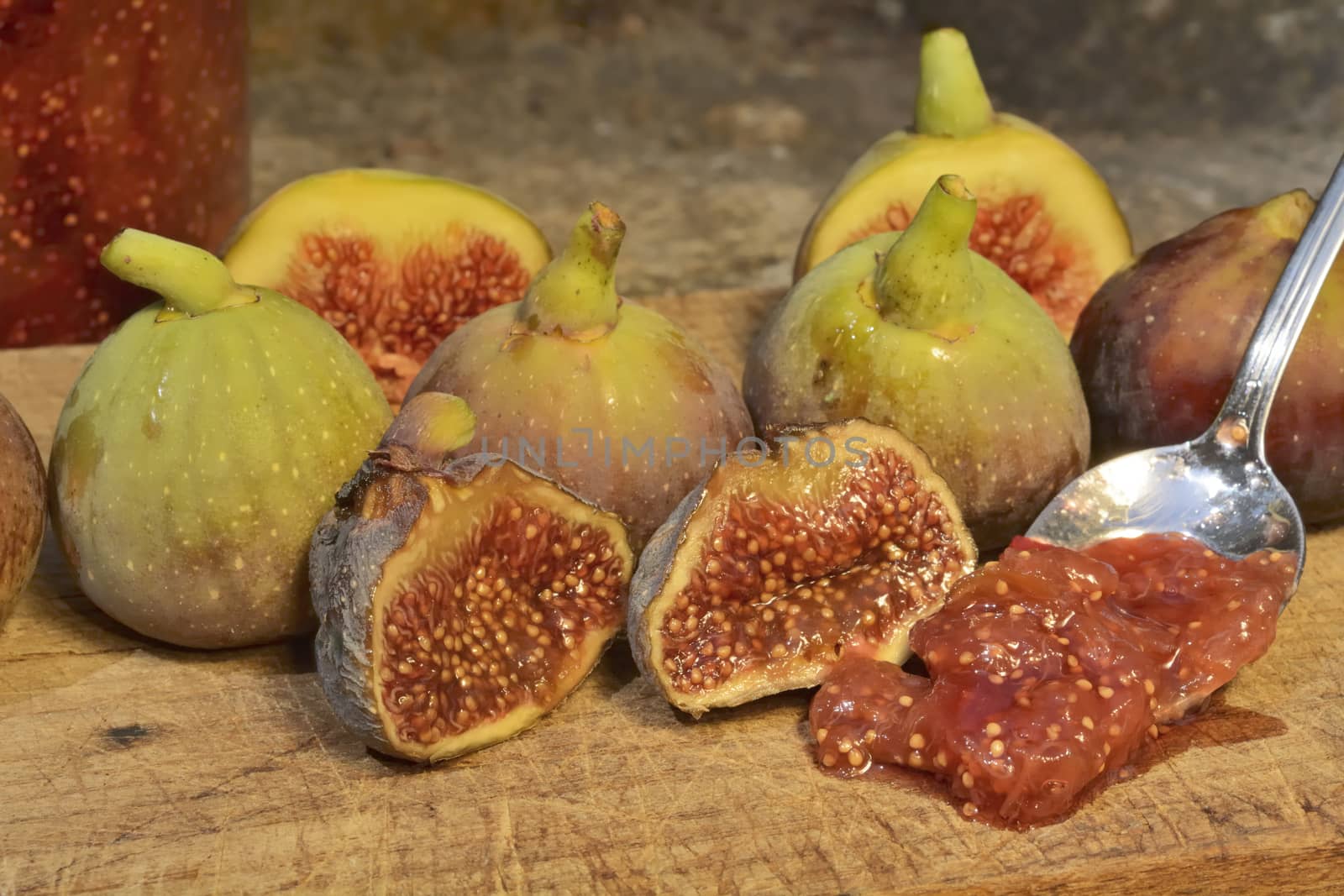 Composition of fig fruits on a wooden board and rocks in the background. Marmalade in the background over a spoon.