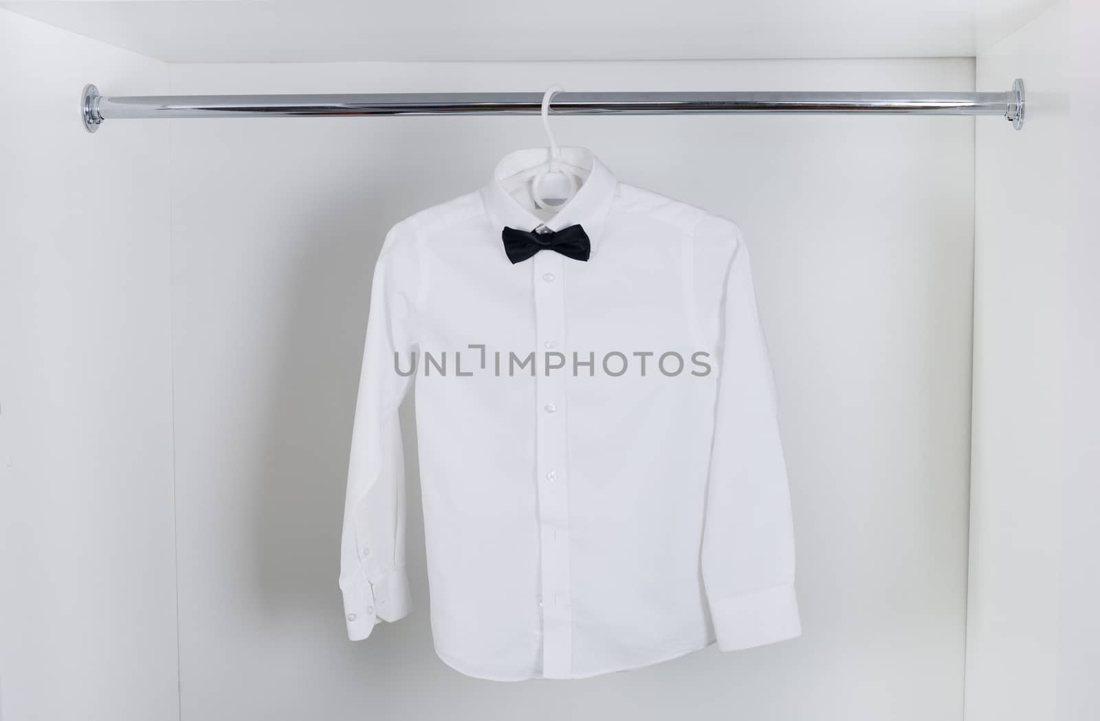 white  men's shirt with black bow tie hanging on hangers in the closet white