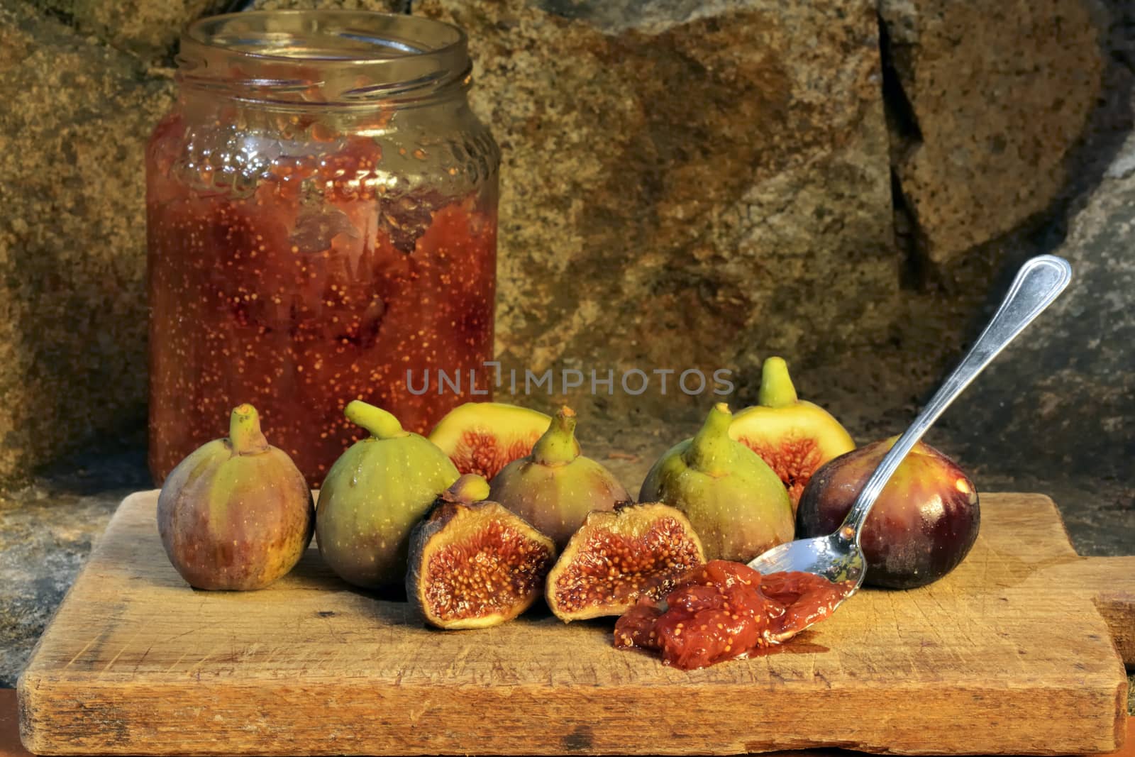 Composition of fig fruits on a wooden board and rocks in the background. Marmalade in the background over a spoon.