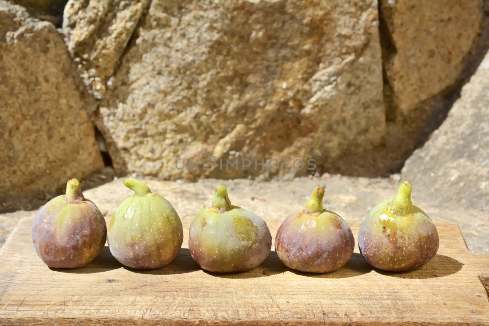 Composition of fig fruits on a wooden board and rocks in the background.
