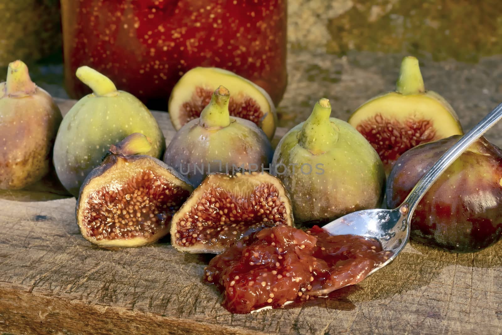 Composition of fig fruits on a wooden board and rocks in the background. Marmalade in the background over a spoon.