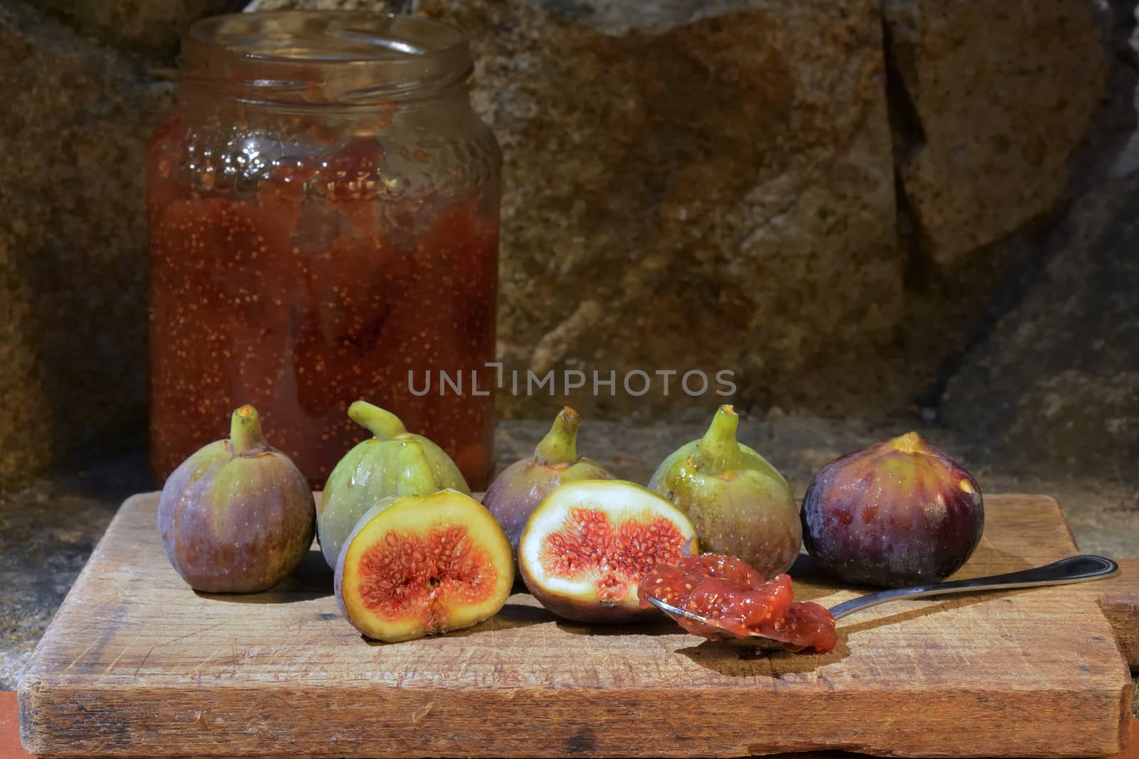 Composition of fig fruits on a wooden board and rocks in the background. Marmalade in the background over a spoon.