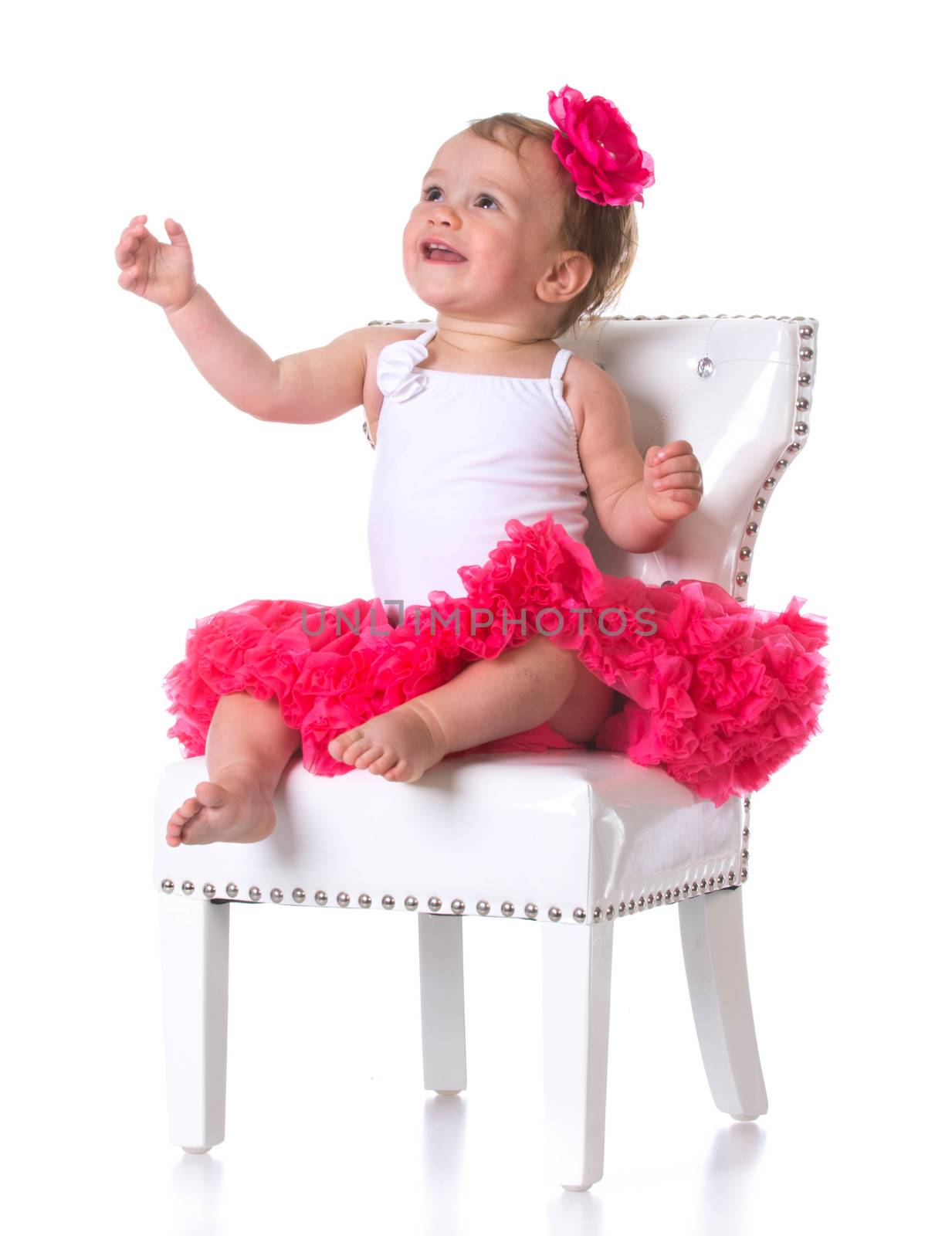 happy one year old girl wearing tutu sitting on a white chair