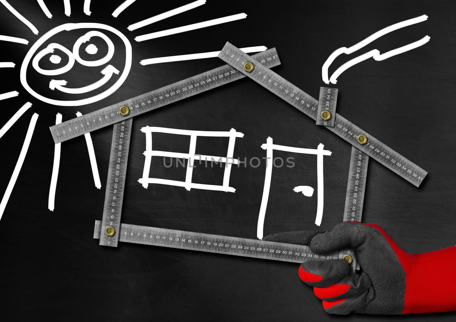 Hand holding a metal meter ruler in the shape of house with sun, door, window and smoke from the chimney. On a blackboard. Concept of house project 