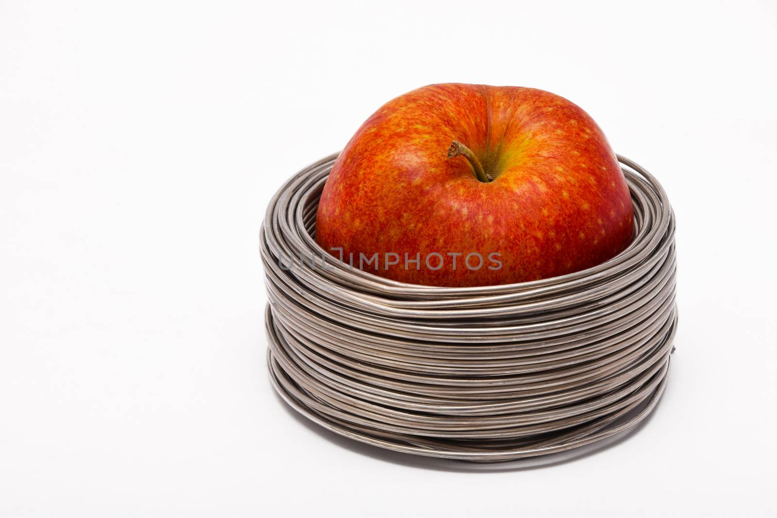 Wired apple: whole red apple in coils of aluminum wire isolated on white background