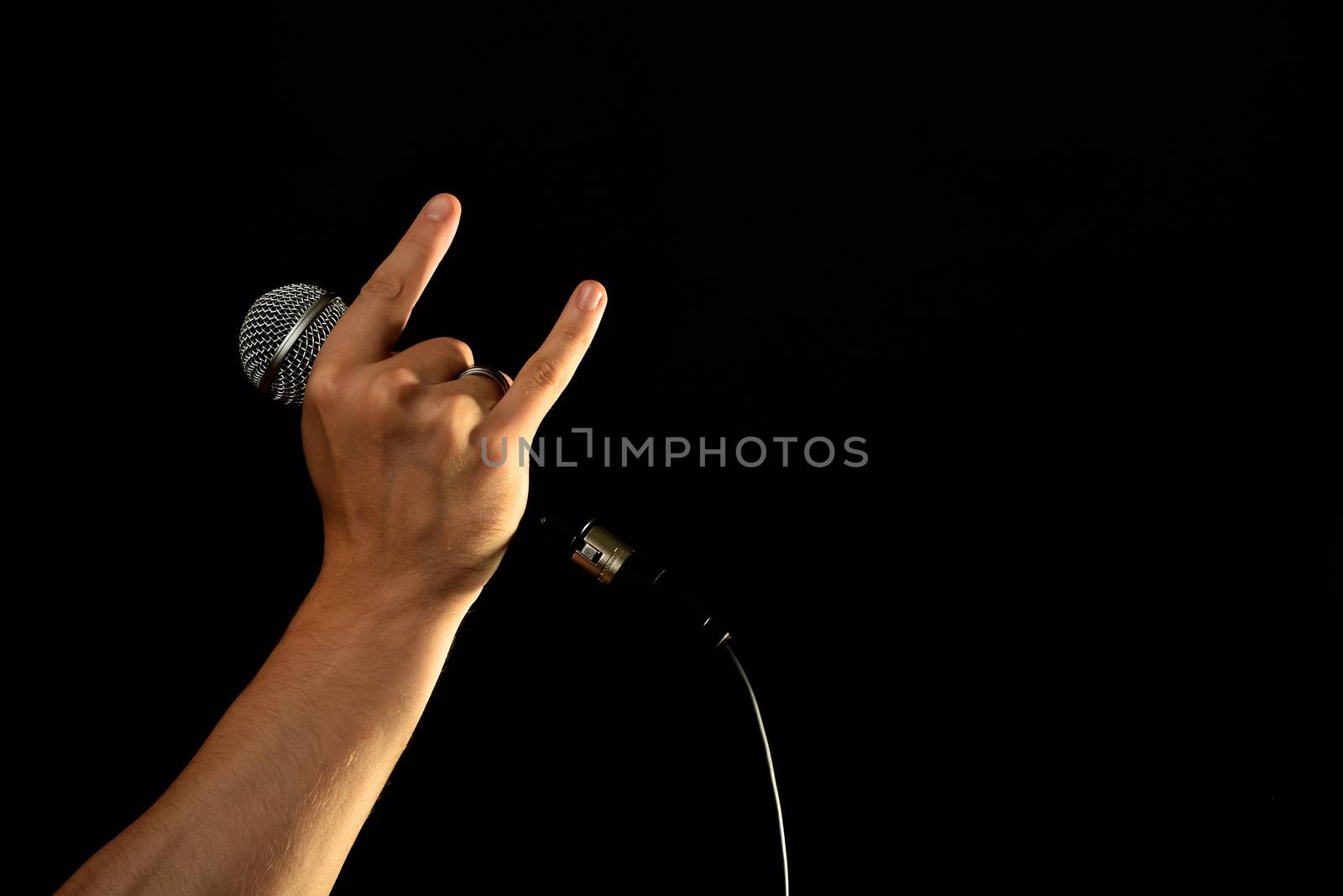 Male hand holding microphone with devil horns rock metal sign isolated on black background
