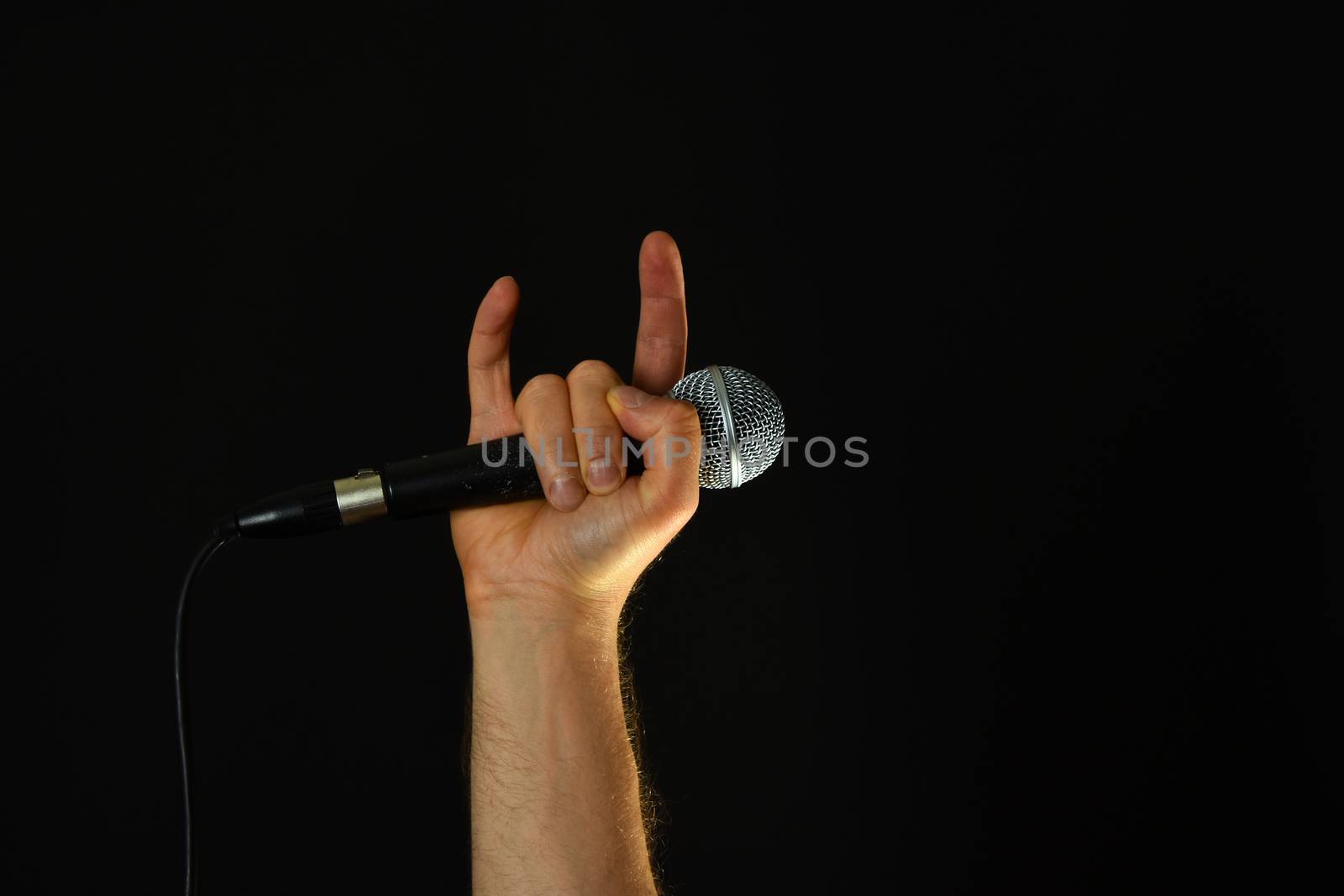 Male hand holding microphone with devil horns rock metal sign isolated on black background