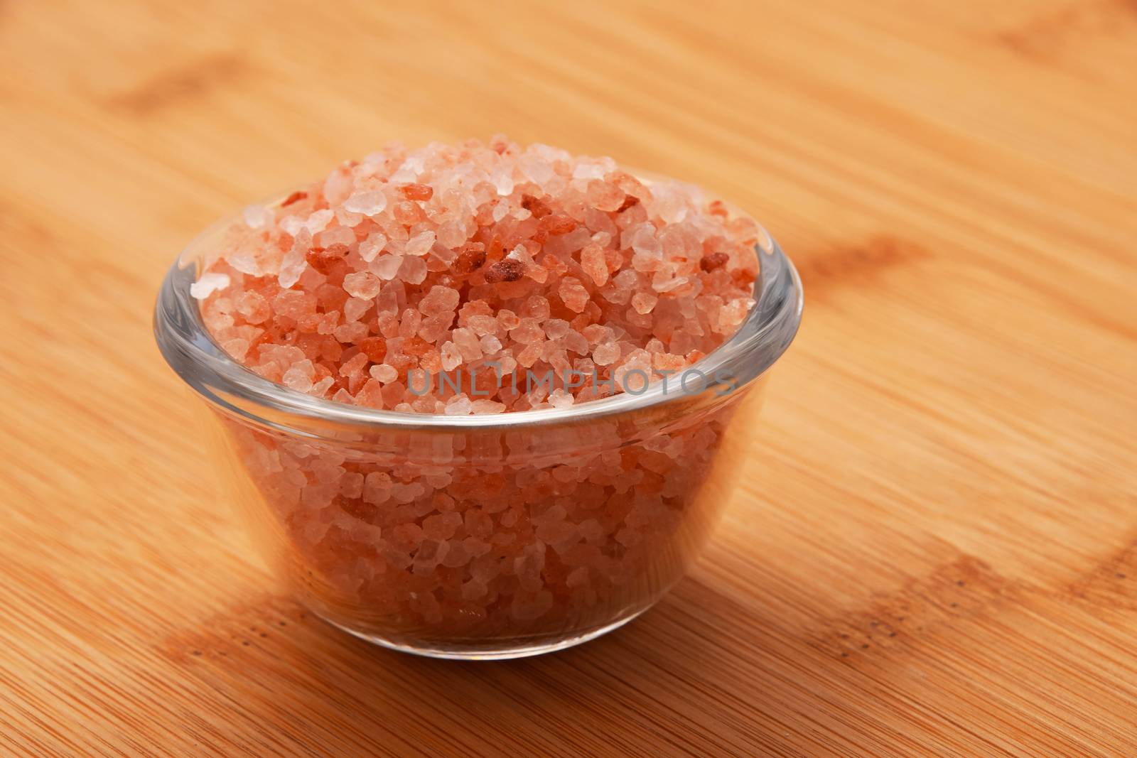 Himalayan pink salt in tiny transparent glass bowl on wooden bamboo background