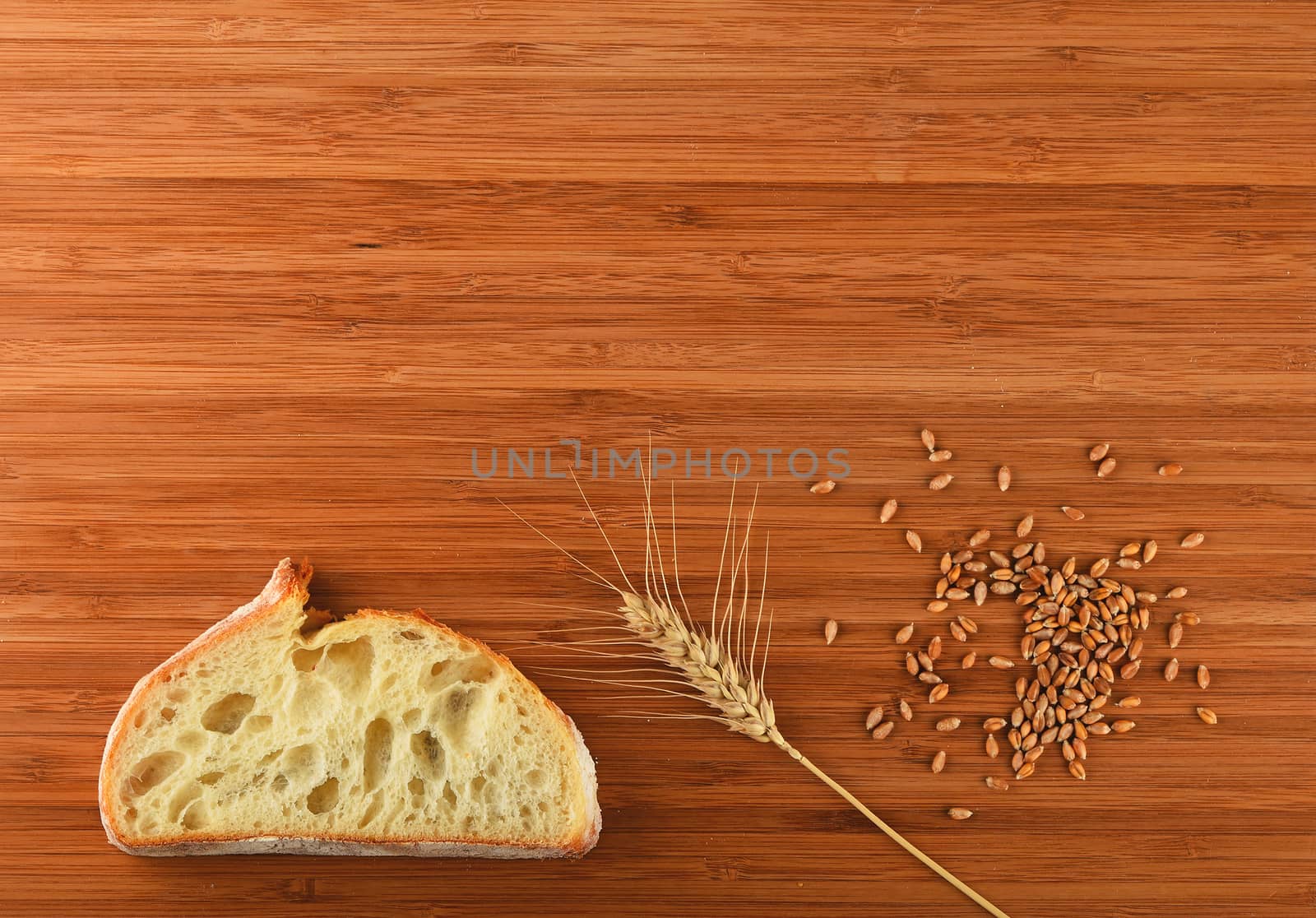 Wooden bamboo cutting board with one wheat ear, handful of ripe grains and a slice of bread - add your text
