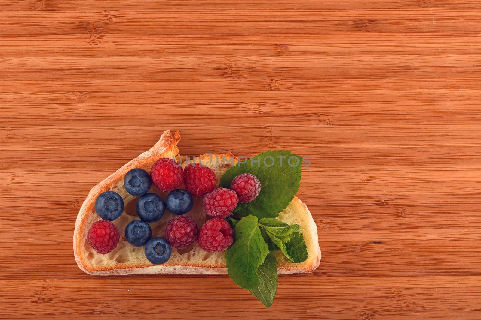 Better than caviar - cutting board with sandwich of mellow blueberries, raspberries and mint leaves on slice of wheat bread