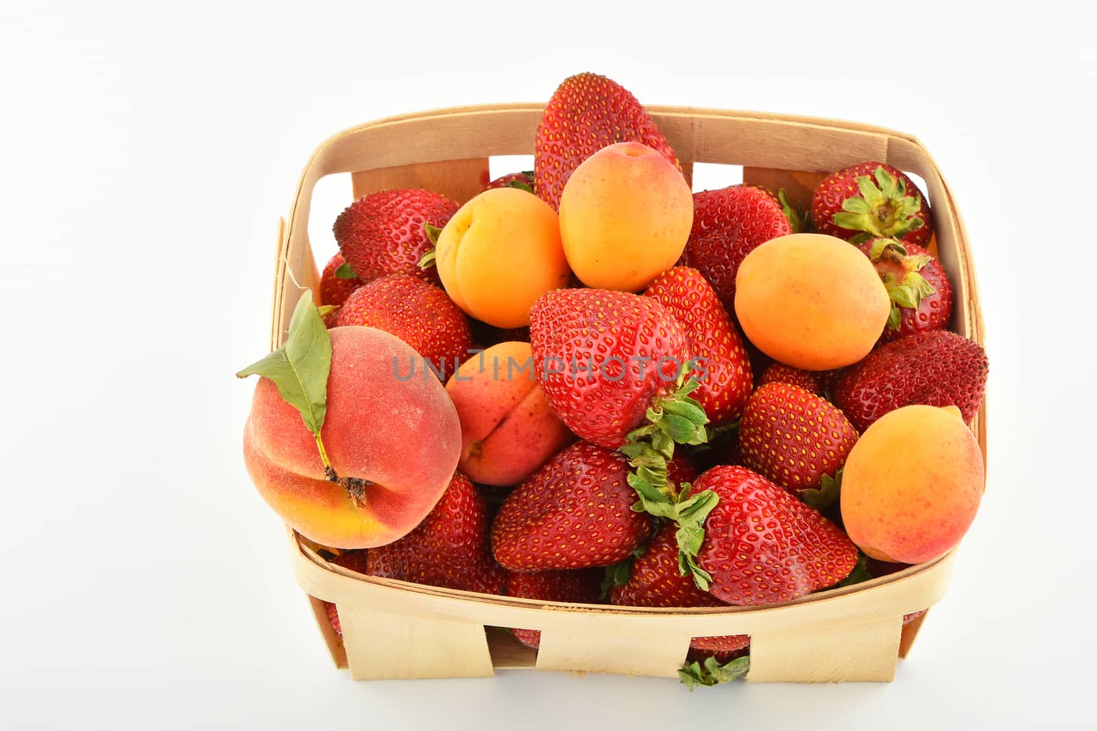 Mellow fresh summer strawberries, apricots and peach in wooden basket isolated on white background