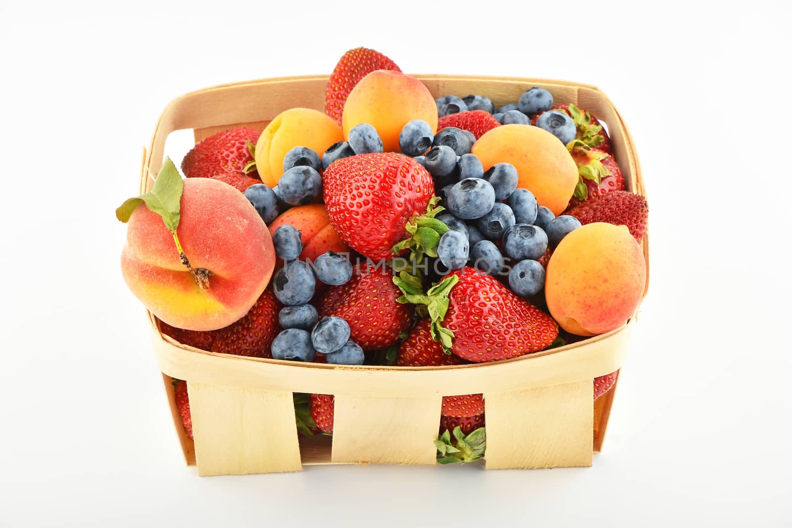 Mellow fresh summer strawberries, blueberries, apricots and peach in wooden basket isolated on white background