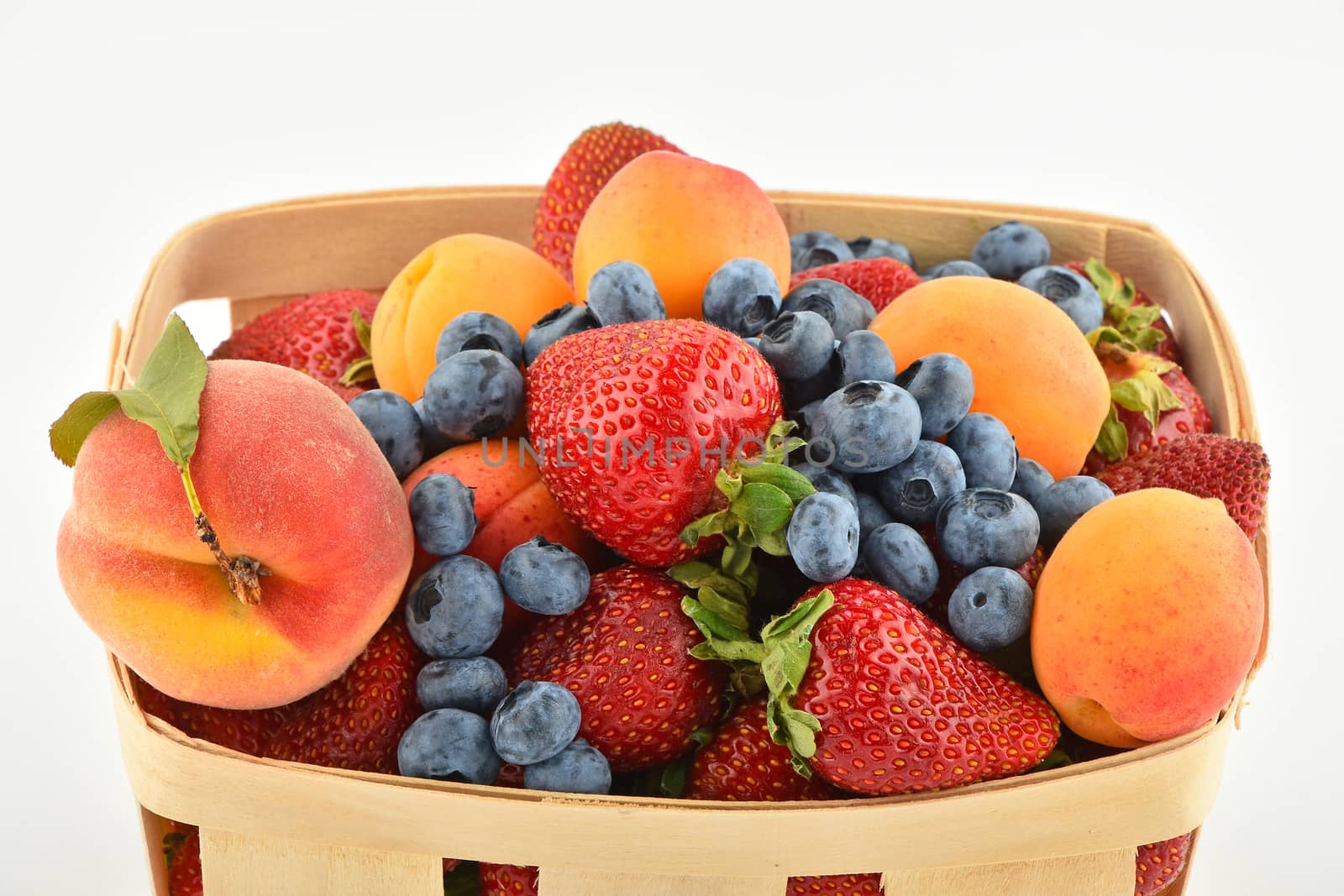 Mellow fresh summer strawberries, blueberries, apricots and peach in wooden basket isolated on white background