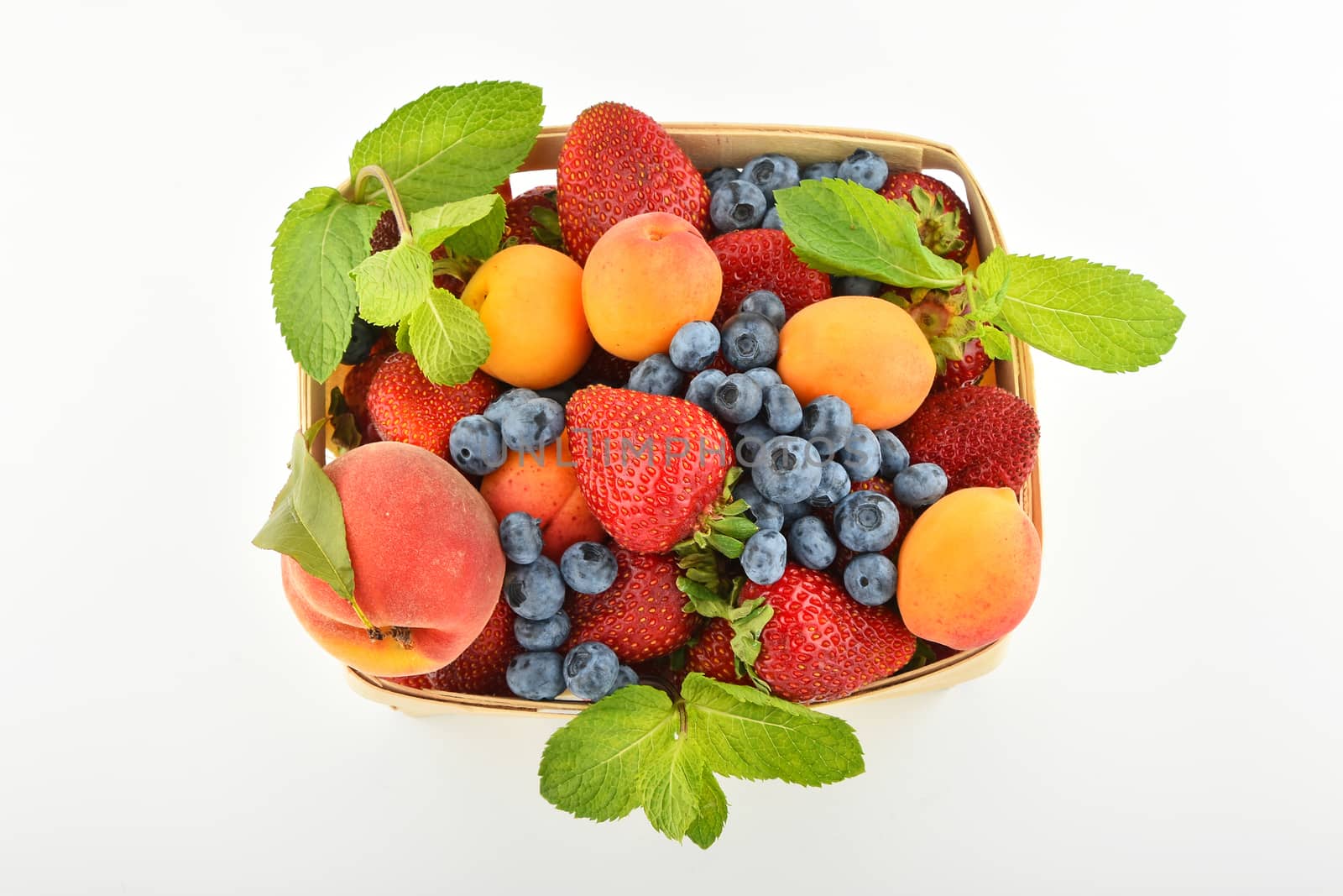 Mellow fresh summer strawberries, blueberries, apricots, peach and mint leaves in wooden basket isolated on white background, top view