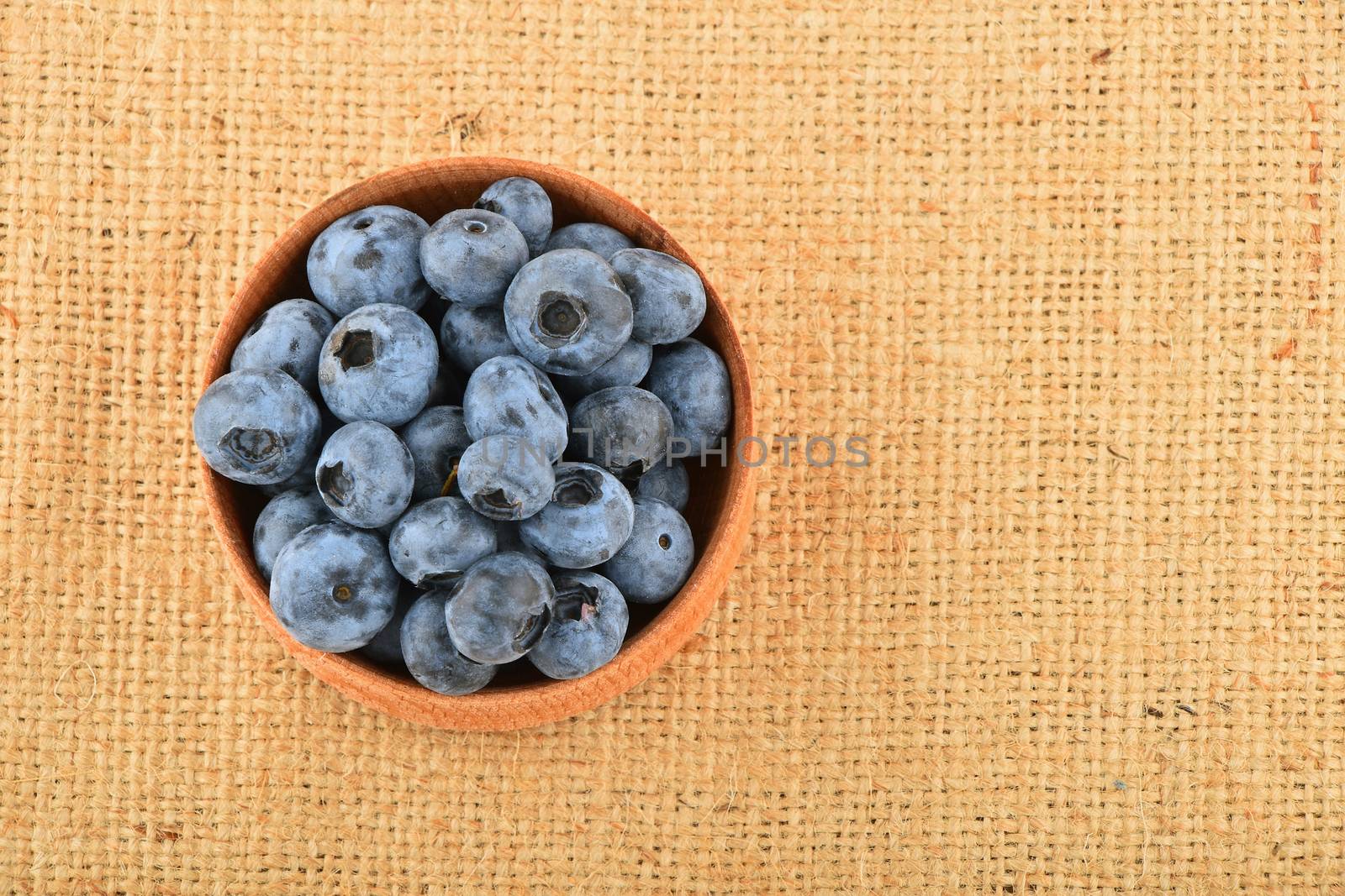Handful of fresh blueberries in handmade wooden bowl on burlap jute canvas, top view