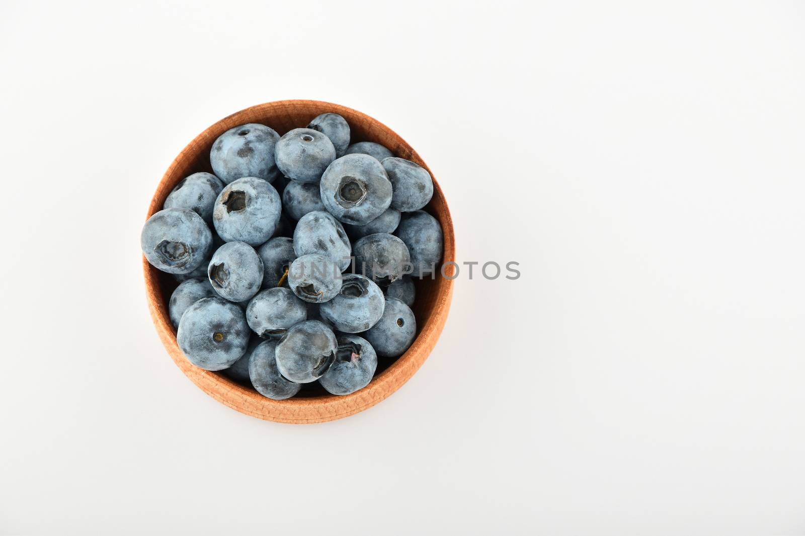 Handful of fresh blueberries in handmade wooden bowl isolated on white, top view