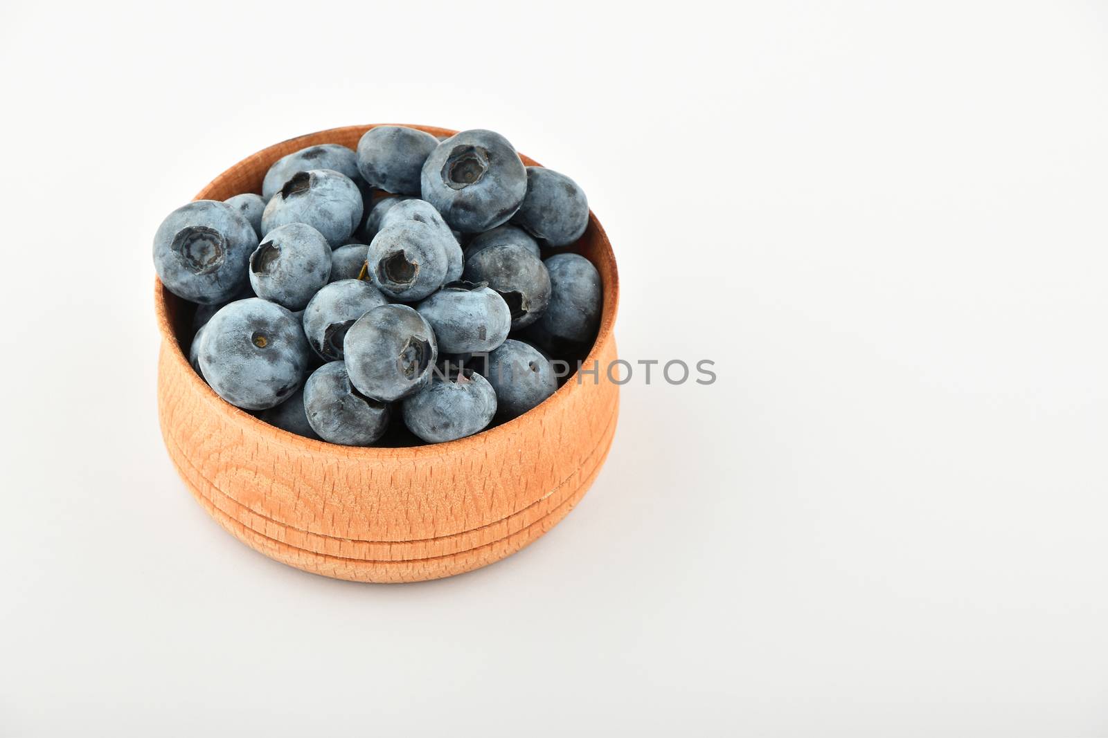 Handful of fresh blueberries in handmade wooden bowl isolated on white