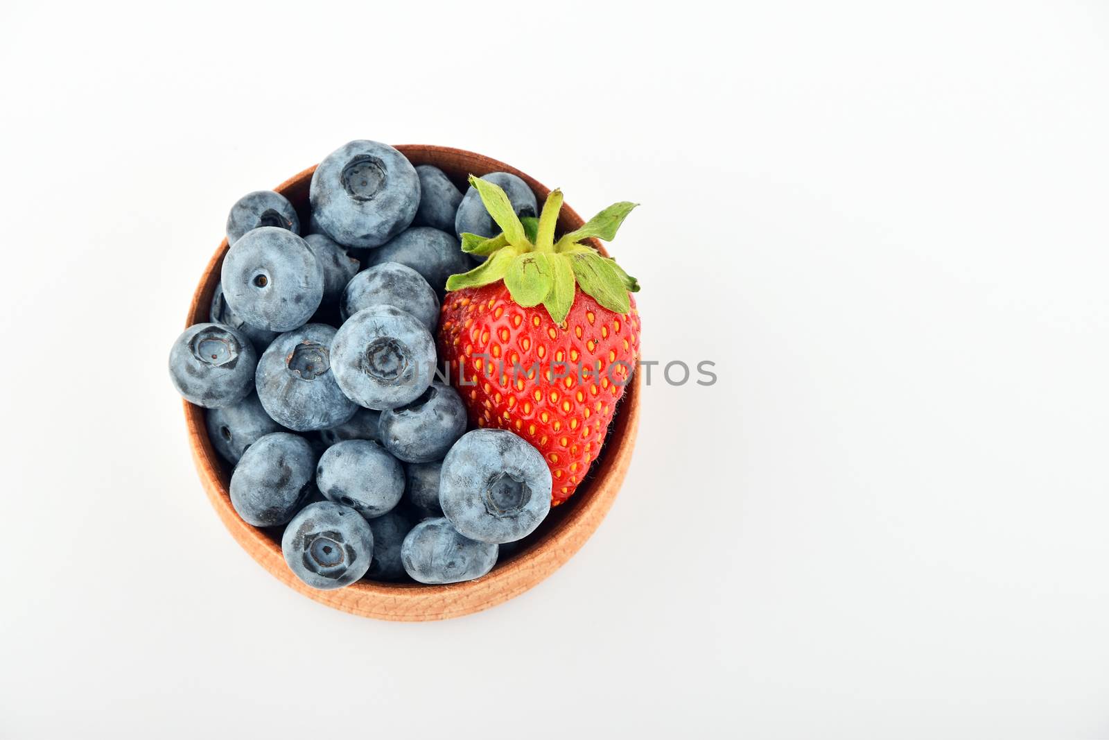 Handful of fresh blueberries and one strawberry in handmade wooden bowl isolated on white, top view