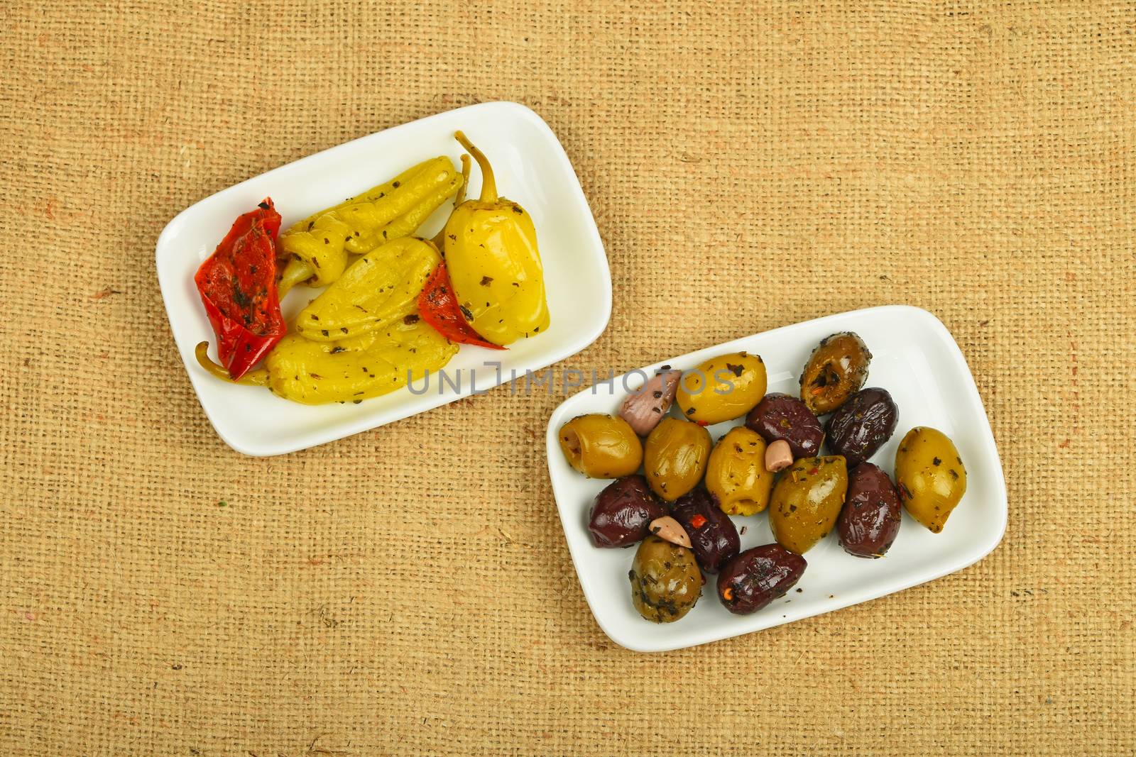 Mediterranean snack of red and green olives and pickled green pepper in two white plates on burlap jute canvas