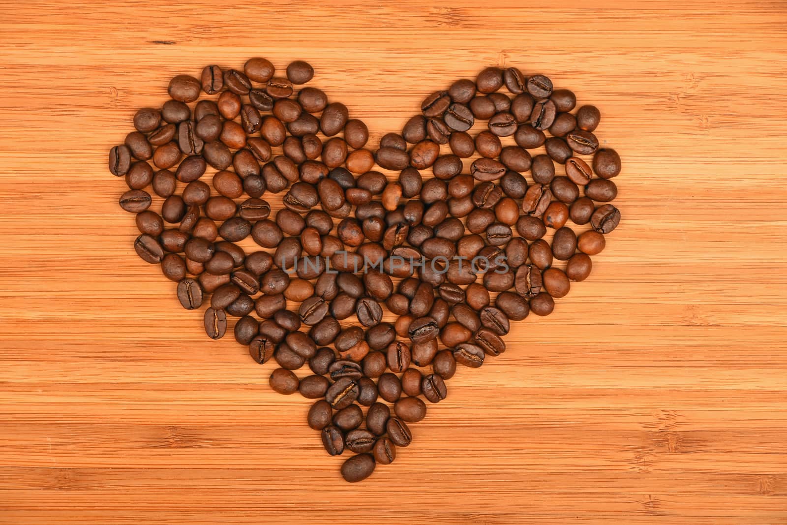 Heart shaped coffee beans of Roasted Arabica espresso beans over wooden bamboo board background
