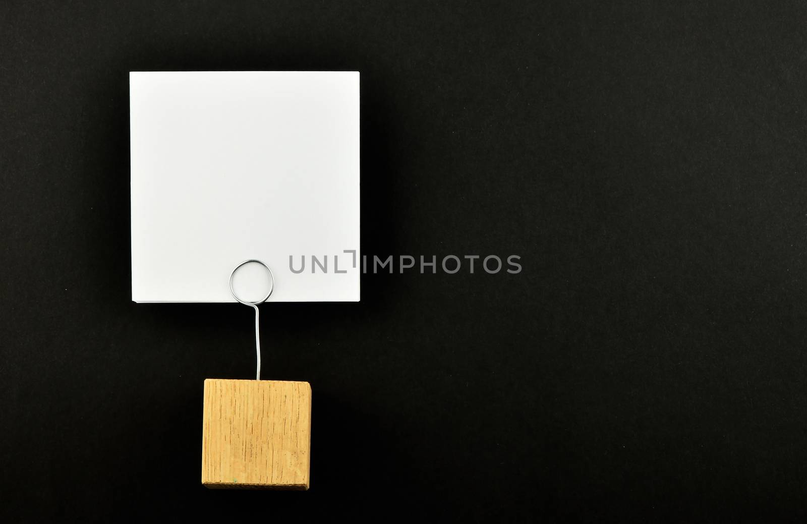 One white paper note with wooden holder isolated at black paper background for presentation