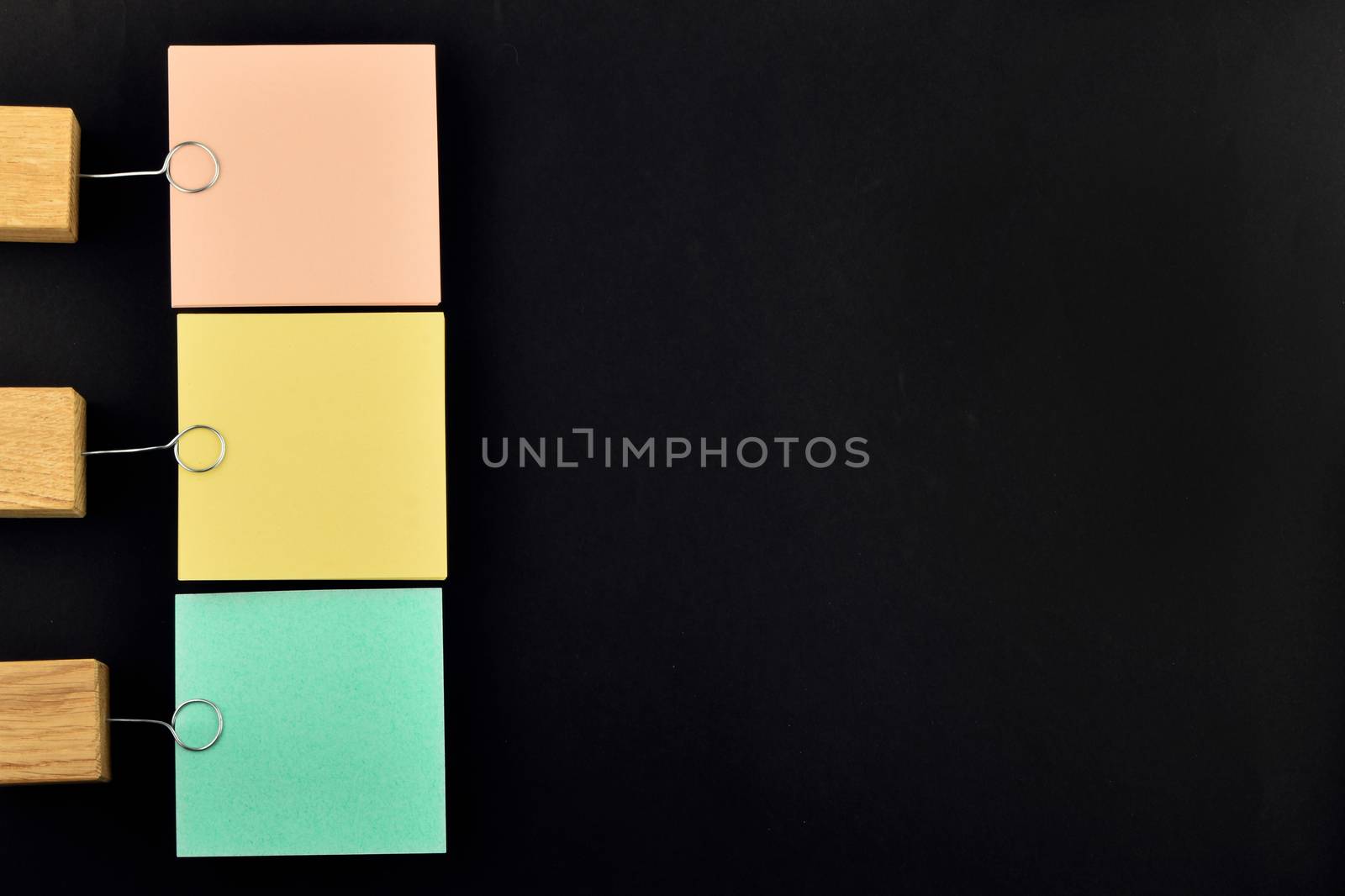 List, three paper notes, green, yellow, pink, with wooden holder isolated on black paper background for presentation