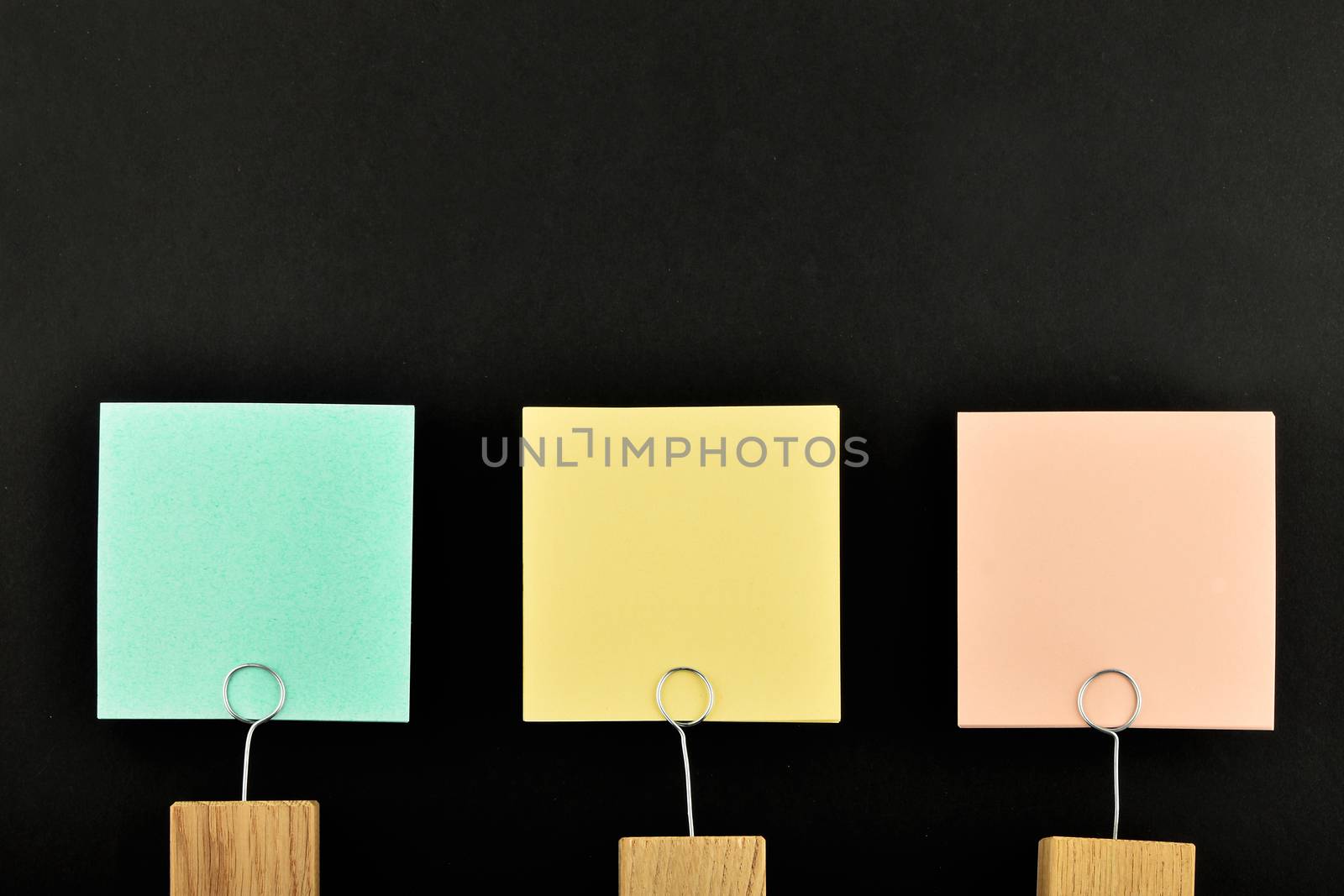 Three paper notes, green, yellow, pink, with wooden holder isolated on black paper background for presentation