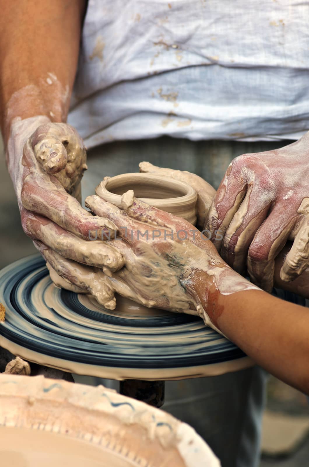 The hands of a potter help the child make a pitcher on a pottery by dolnikow