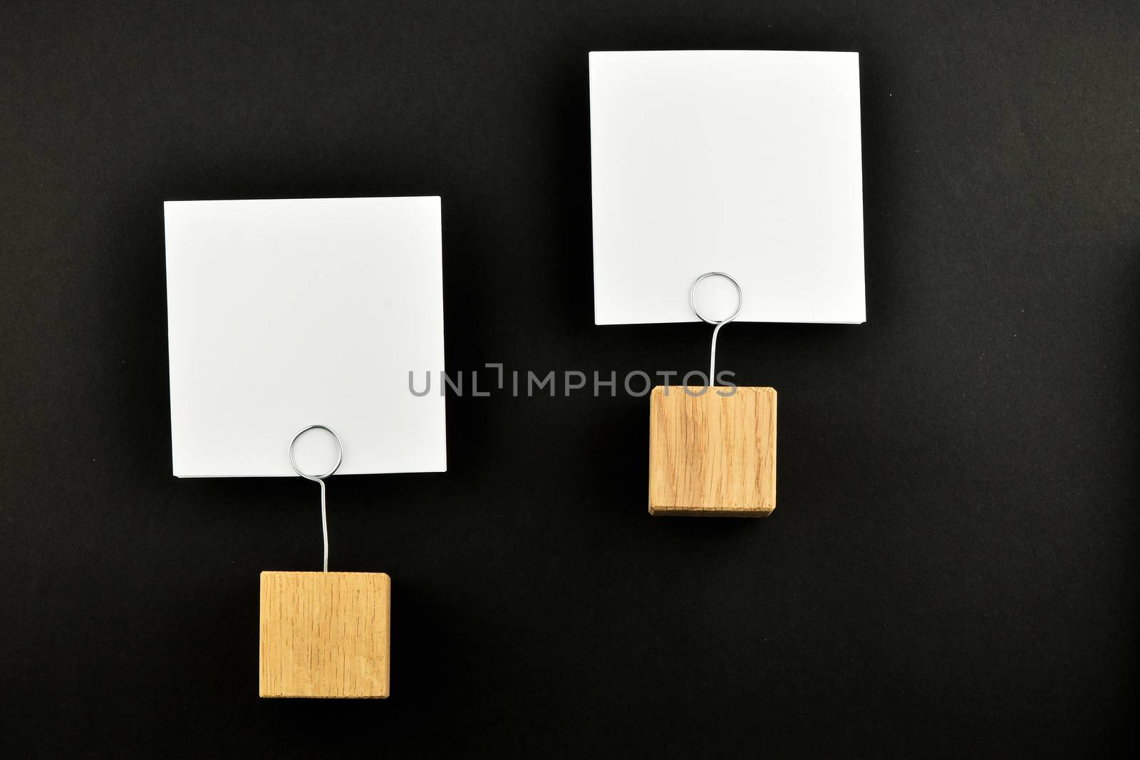 Two white paper notes at different levels with wooden holders isolated at black paper background for presentation
