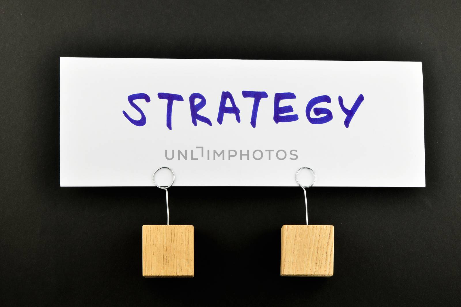Strategy, One big white paper note with two wooden holders isolated on black paper background for presentation
