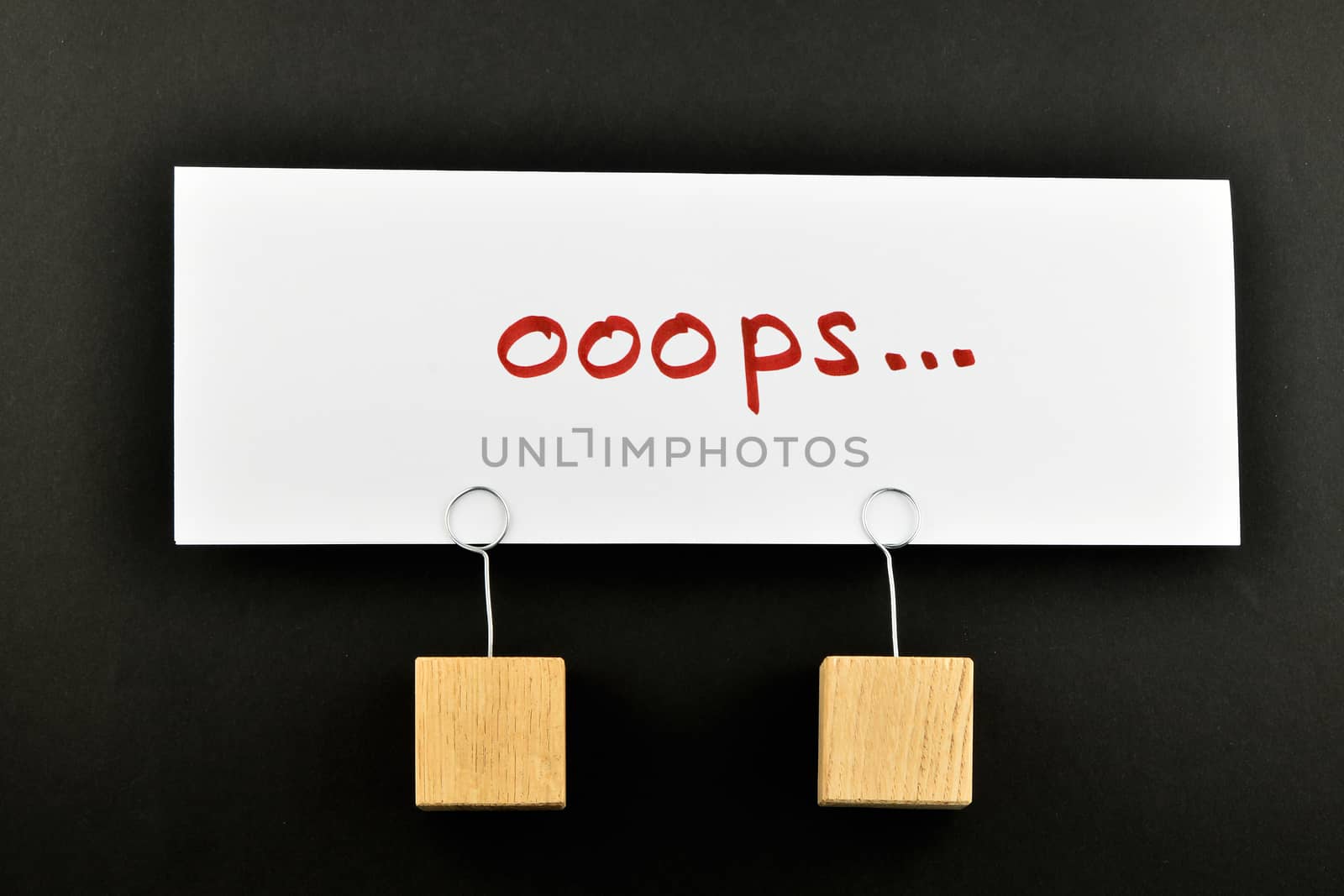 Oops, one big white paper note with two wooden holders isolated on black paper background for presentation
