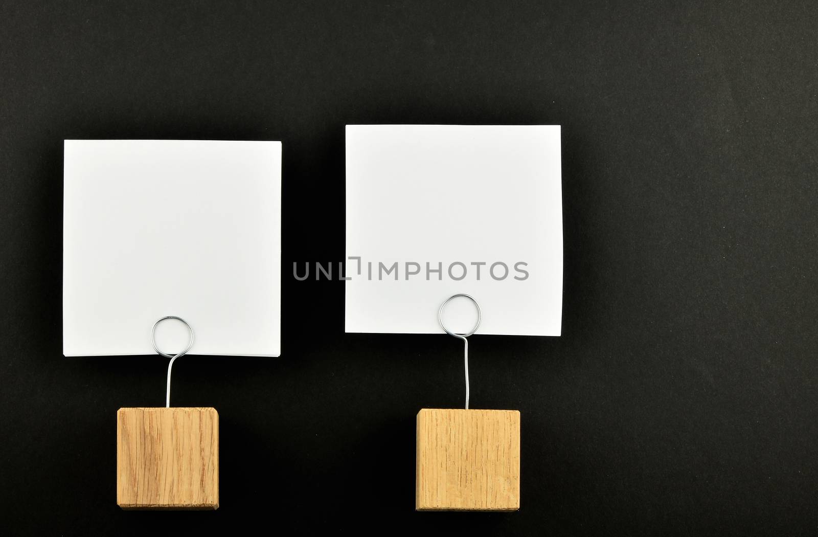 Two white paper notes with wooden holders isolated at black paper background for presentation