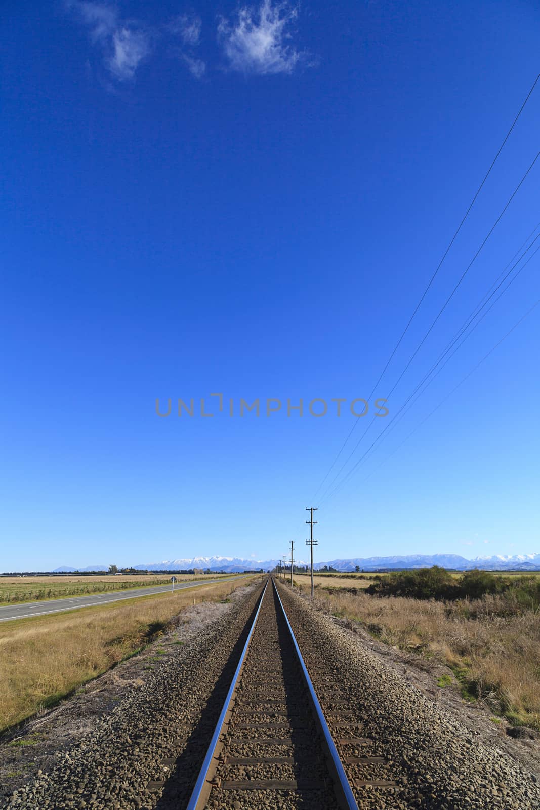Rural railway straight to horizon under blue sky in Canterbury region, South Island, New Zealand.