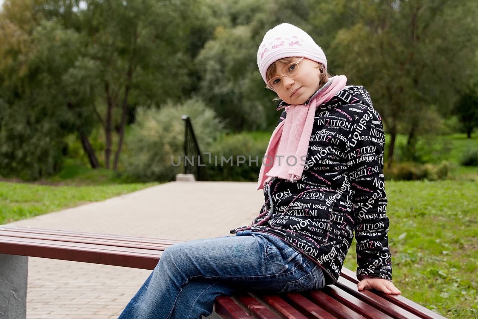 Pretty  child girl in glasses sits on a Park bench