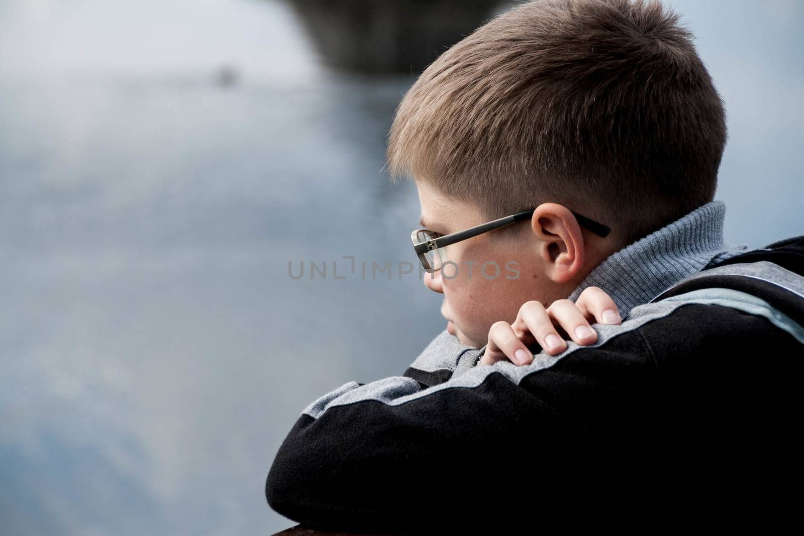 the teenager is situated on the bank of the river. look aside. selective focus